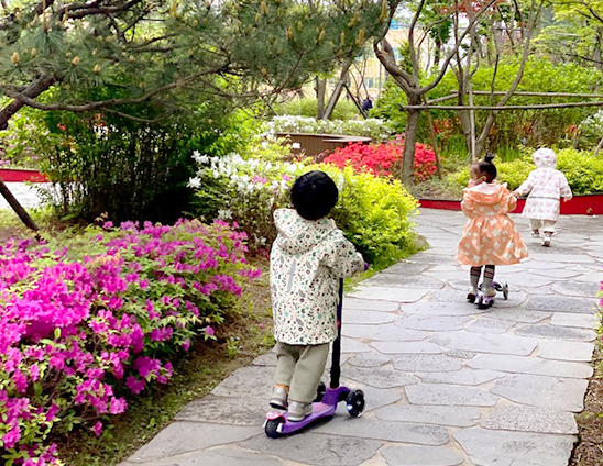 봄 꽃이 활짝 핀 단지 에서 킥보드를 타는 아이들의 뒷모습 - 자이브랜드매거진-비욘드아파트먼트-한강센트럴자이-봄 산책