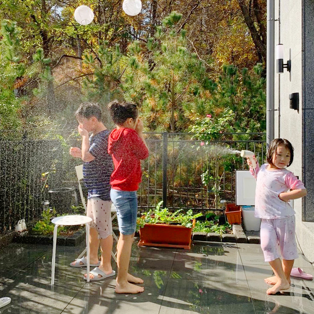 집 테라스에서 물 호수를 쏘며 물놀이를 즐기고 있는 어린 아이들-삼송자이더빌리지-자이매거진-비욘드아파트먼트
