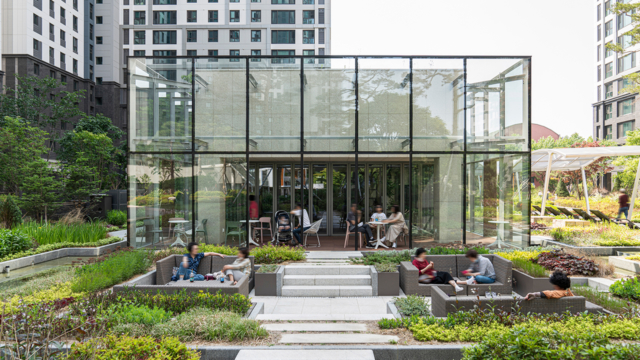 과천자이 아파트 커뮤니티 시설 티하우스. 유리로 되어 개방감이 느껴지는 티하우스와 주변의 정원 벤치에 사람들이 담소를 나누고 있다.-자이매거진-비욘드아파트먼트-인터뷰-커뮤니티시설