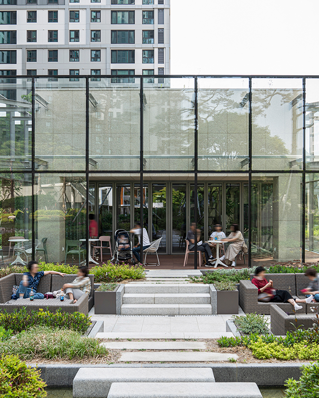 과천자이 아파트 커뮤니티 시설 티하우스. 유리로 되어 개방감이 느껴지는 티하우스와 주변의 정원 벤치에 사람들이 담소를 나누고 있다.-자이매거진-비욘드아파트먼트-인터뷰-커뮤니티시설