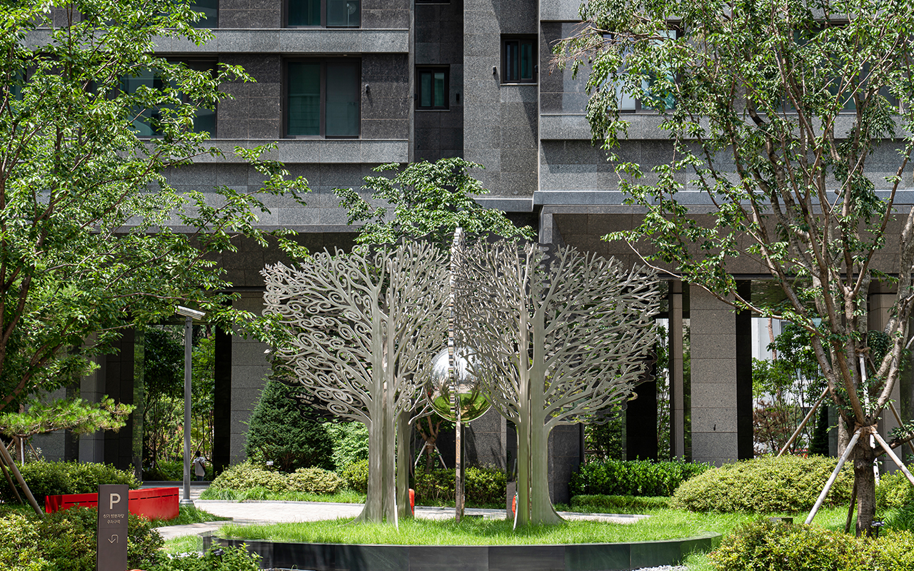 자이매거진-비욘드아파트먼트-서초그랑자이-조경-서울 서초구에 위치한 서초그랑자이 아파트 건물을 배경으로 한 정원의 나무들과 나무 모양의 금속 조형물