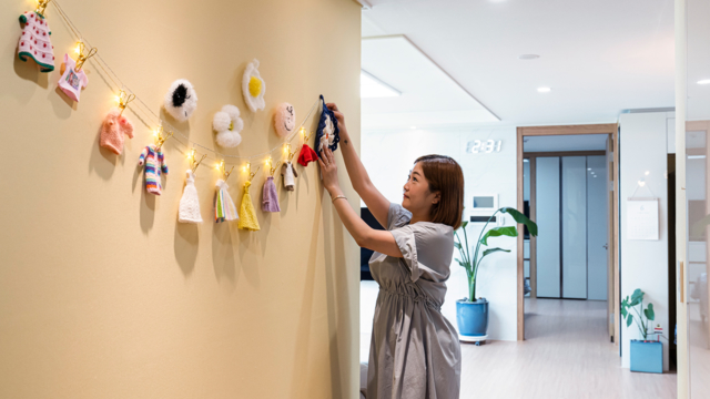 자이매거진-비욘드아파트먼트-평택센트럴자이-경기도 평택시 평택센트럴자이 아파트 거실 풍경. 노란 컬러 벽에 주부가 직접 뜨개질한 뜨개옷과 수세미에 조명을 더해 벽면을 꾸미고 있다.