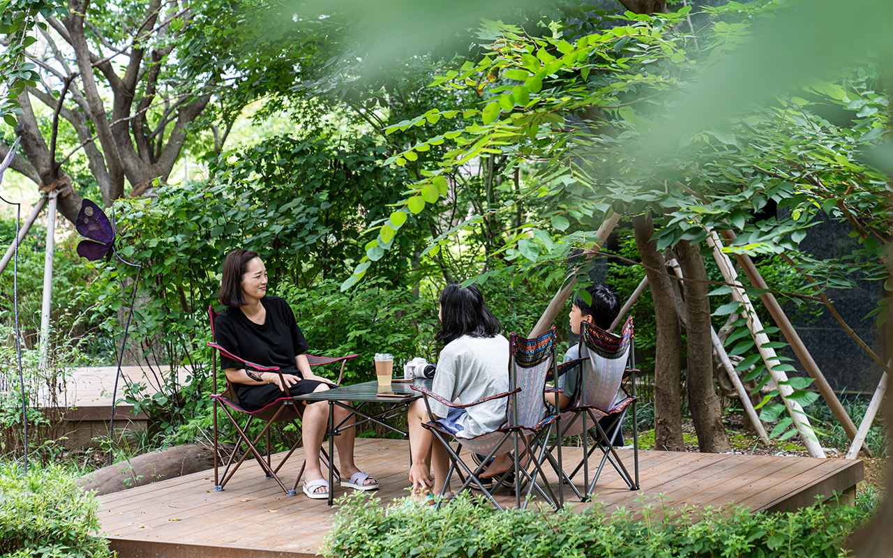 자이매거진-비욘드아파트먼트-고덕자이-나무로 만든 캠핑 데크 위에 테이블을 펼쳐 놓은 가족