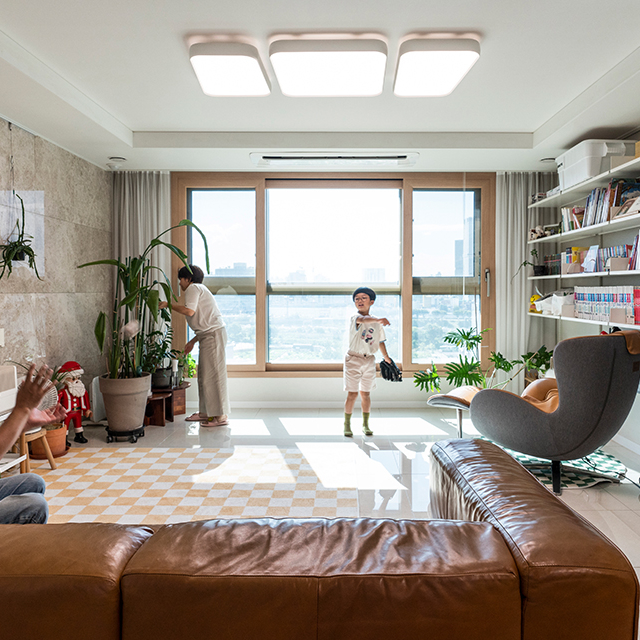 자이매거진-비욘드아파트먼트-아파트 거실에서 식물을 돌보는 엄마와 공놀이를 하는 아빠와 아들
