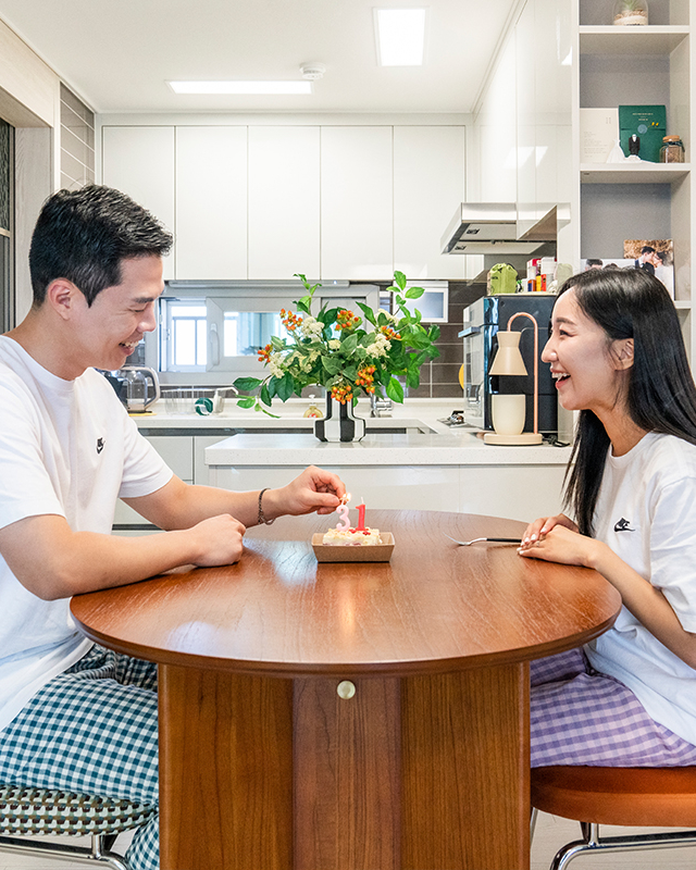 자이매거진-비욘드아파트먼트-아파트 주방의 테이블에서 결혼기념일 케익에 촛불을 켜고 있는 젊은 커플