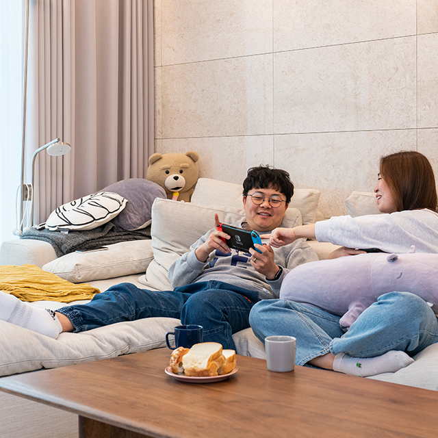 자이매거진-비욘드아파트먼트-아파트 거실의 소파에 부부가 누워 닌텐도 게임을 즐기고 있다